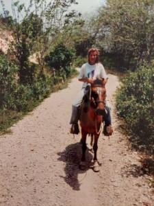 Henkilö ratsastaa hevosella tiellä aurinkoisessa maisemassa.