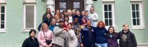 Ihmisiä asettauneina ryhmäkuvaan rakennuksen oven edustalla. People posing in a group photo in front of of a building's door.