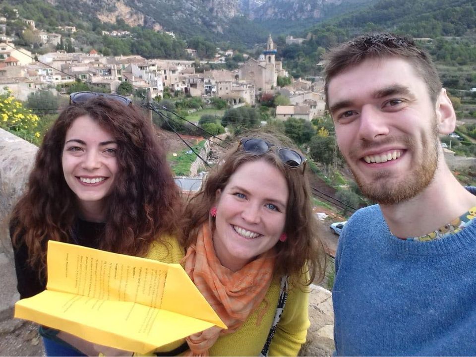 Three smiling people looks at the camera, one of them is holding a paper plane in their hands, in the background, a mountaneus city view.