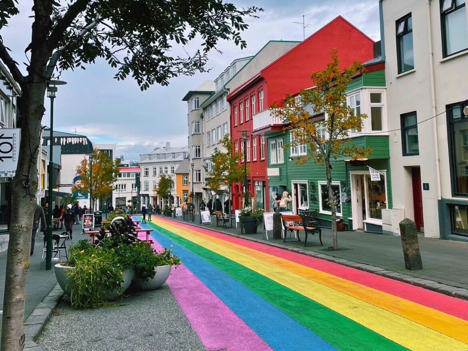 A street painted with colors of the rainbow, on both sides of the street there are buildings and a couple of people.