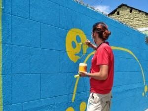 A person painting a picture with yellow paint on a blue wall.